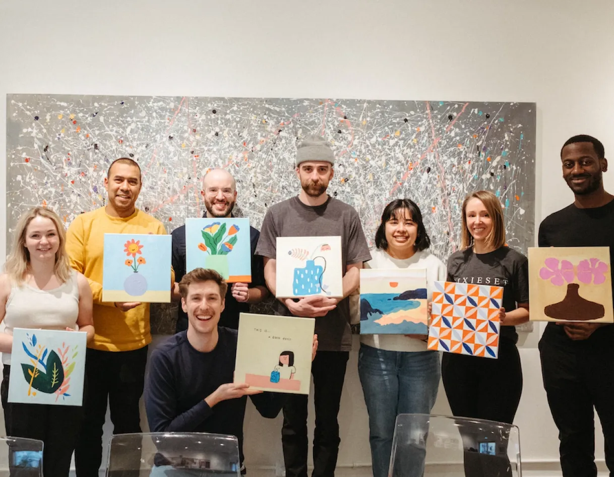 Pixieset team members holding up colorful paintings, reflecting the company’s craftsmanship values and creator-first culture highlighted in the Careers page message.
