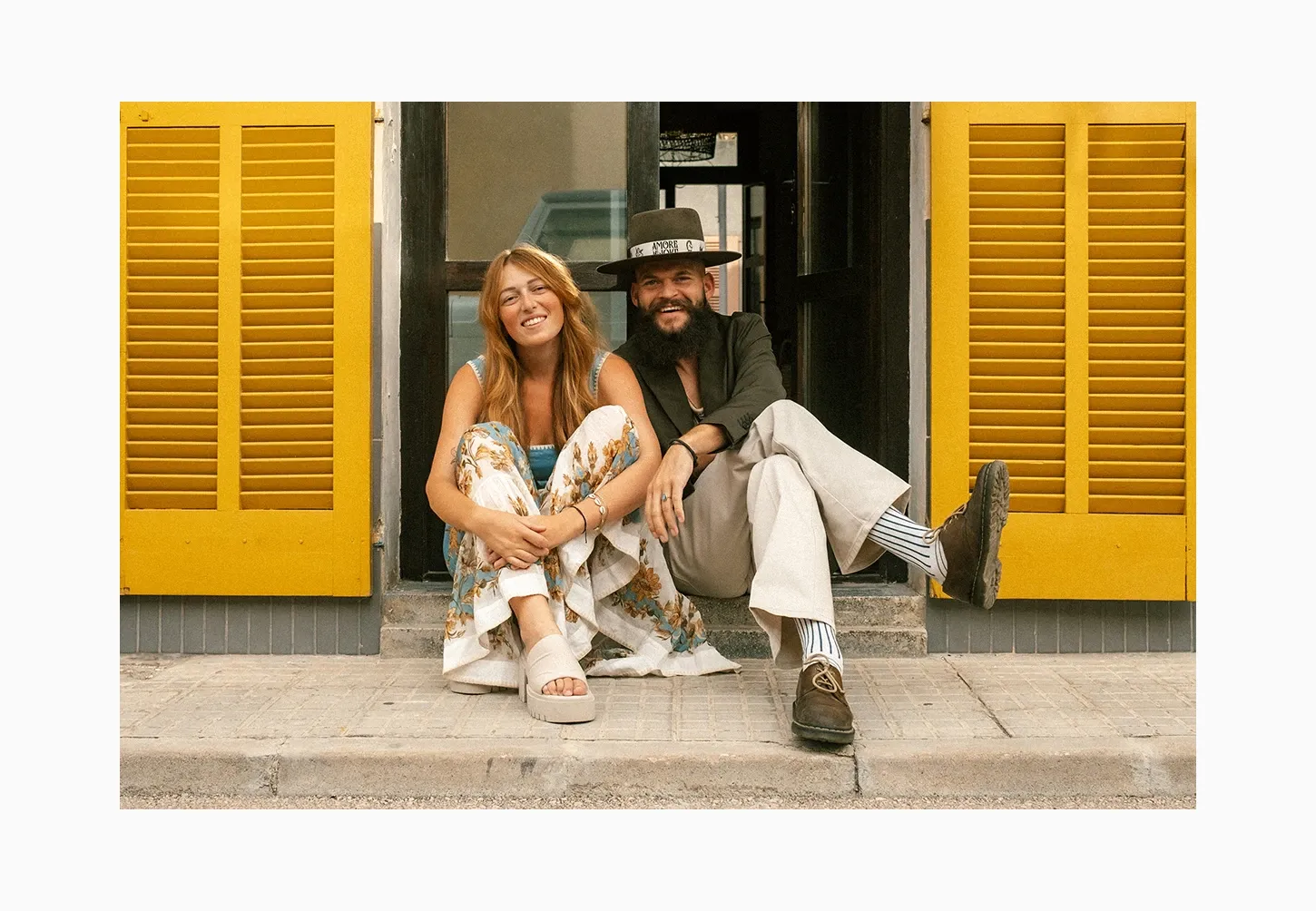 Casual lifestyle portrait of a Chris & Ruth sitting on a colorful doorstep with bright yellow shutters, perfect for engagement or personality photography portfolio