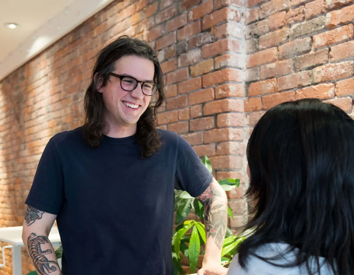 A photo highlighting Pixieset's small but impactful team, with a smiling team member with tattoos and glasses chatting in the office