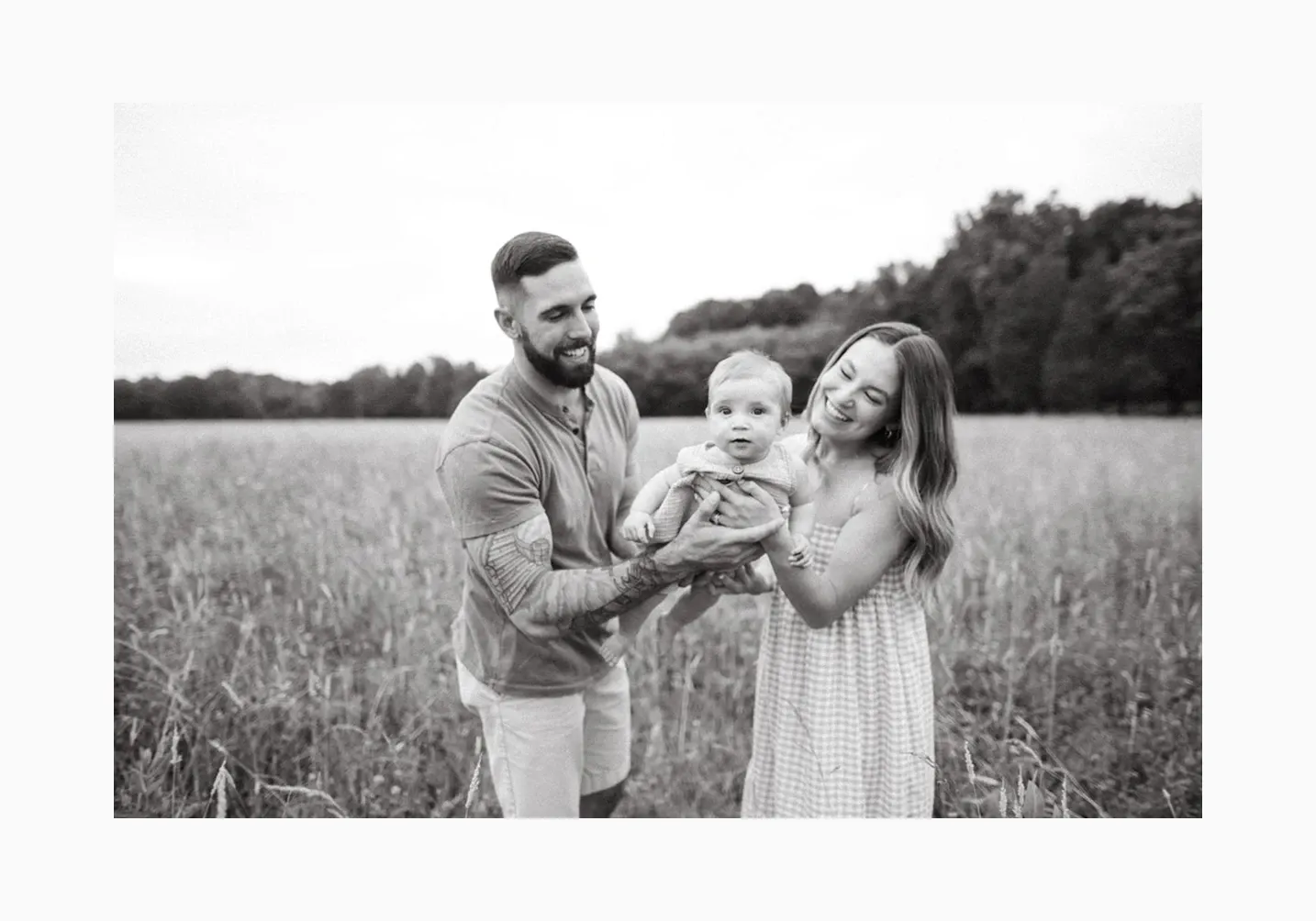 Black and white photo of parents holding baby in a scenic field, capturing timeless and emotional family photography - photographed by Megan Black