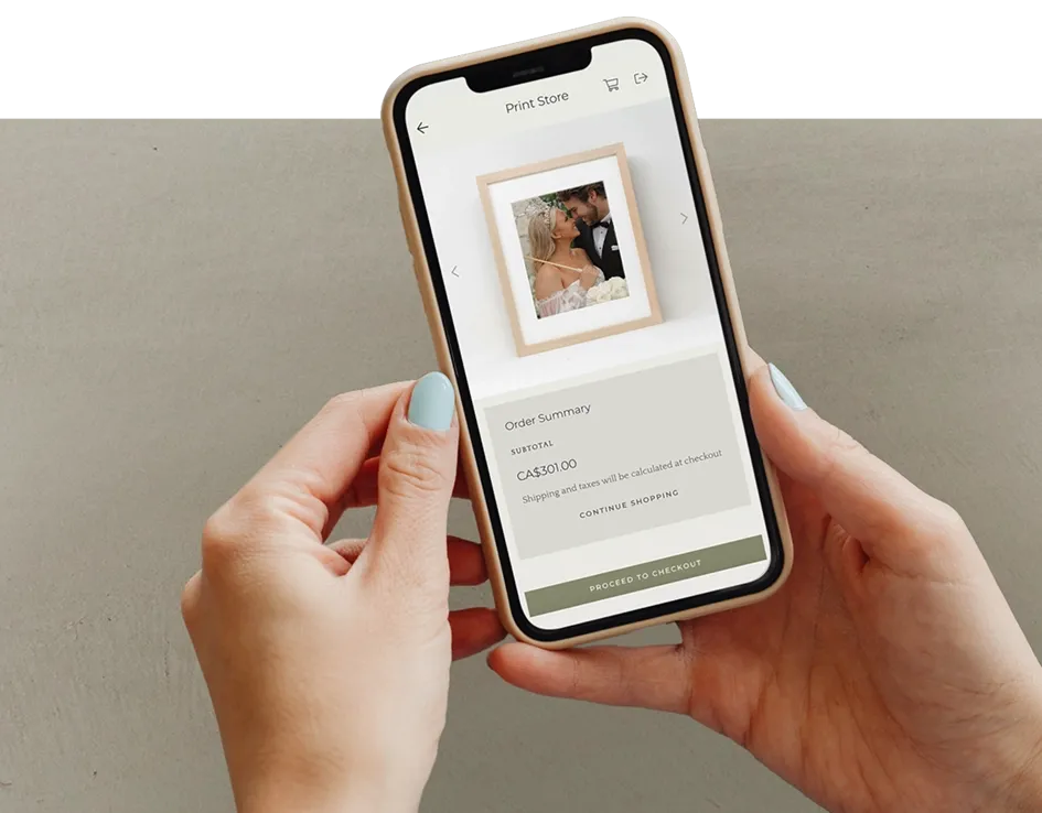 Hands holding a smartphone displaying Pixieset Print Store checkout screen with a framed wedding photo.